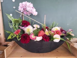 Composition florale moderne en coupe noire avec orchidées roses, dahlias rouges et feuilles de monstera, artisan fleuriste Morbihan