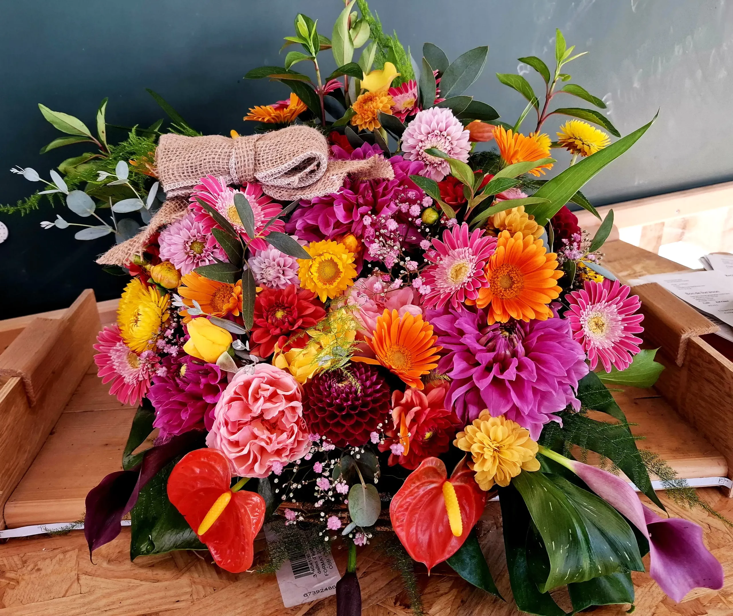 Grande composition florale festive et colorée avec anthuriums, gerberas et nœud en toile de jute, fleuriste événementiel Languidic