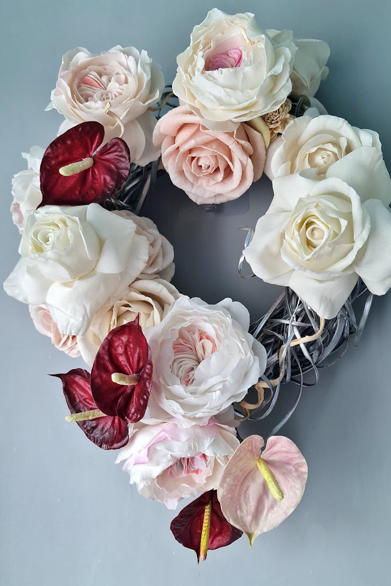 Heart-shaped wreath with white and pink roses and anthuriums on a gray background.