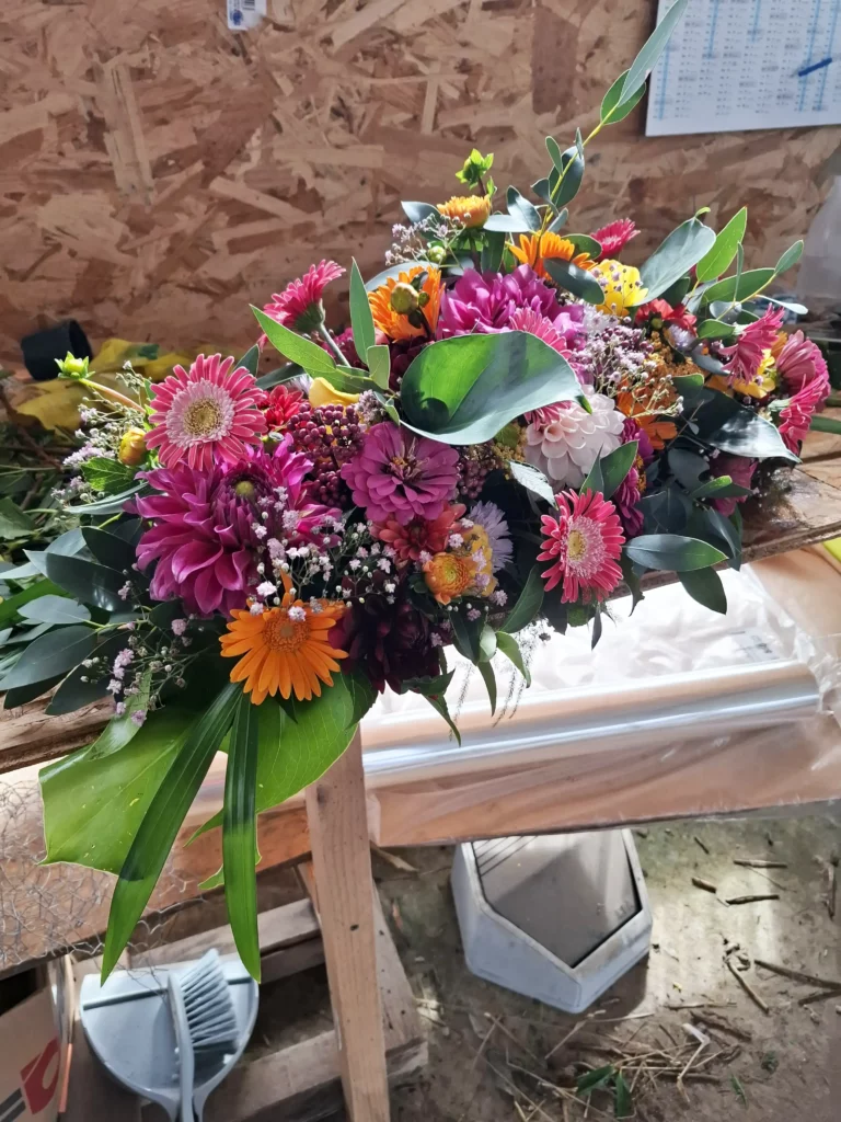 Raquette de deuil pour dessus de cercueil en cours de création à l'atelier avec dahlias et gerberas colorés, fleuriste funéraire Languidic