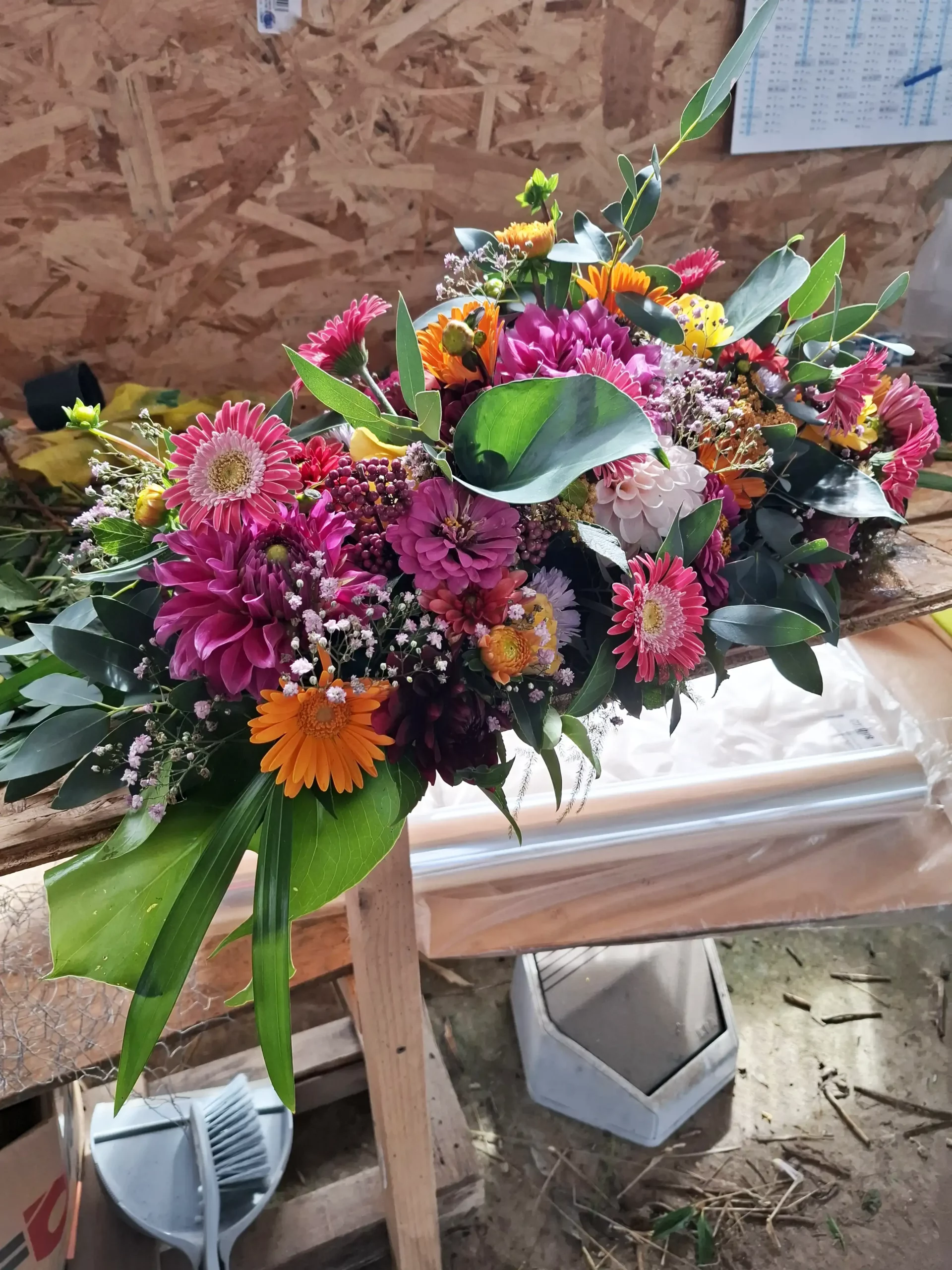 Raquette de deuil pour dessus de cercueil en cours de création à l'atelier avec dahlias et gerberas colorés, fleuriste funéraire Languidic